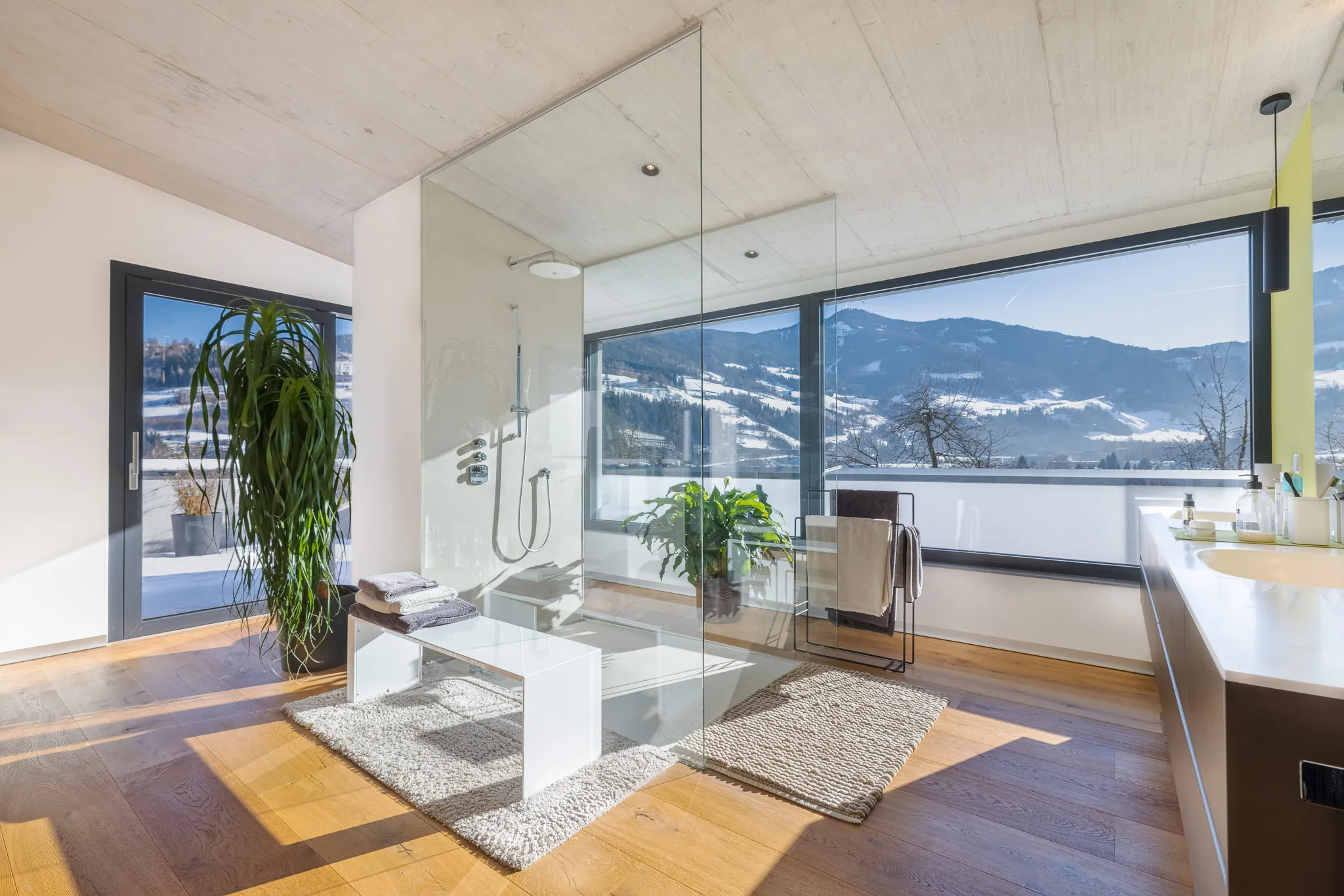 Badezimmer mit gläserner Dusche und großem Fenster mit Bergblick